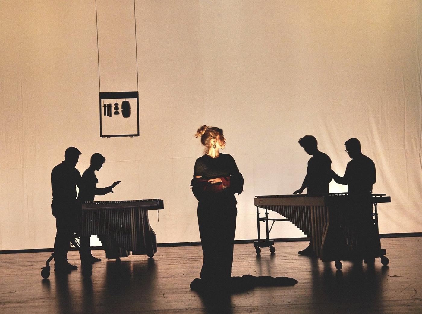 Percussionisti in controluce alle marimbe e un'attrice al centro